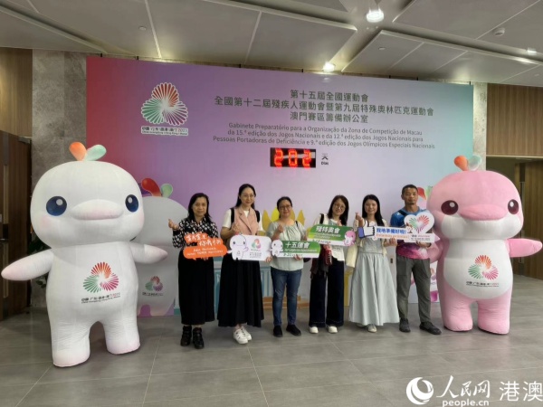 圖為參加培訓(xùn)的澳門(mén)賽區(qū)部分志愿者在倒計(jì)時(shí)牌前，與賽事吉祥物合影。人民網(wǎng)記者 富子梅攝