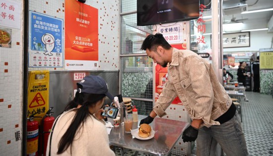 12月13日，邱志暉（右）在其創(chuàng)辦的茶餐廳珠海夏灣店里給顧客送餐。新華社記者 鄧華 攝
