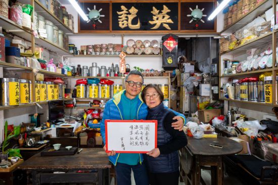 12月18日，澳門英記茶莊的傳承人盧石麟（左）與夫人在展示祝福語。