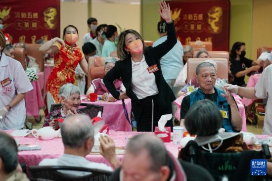 5月24日，在香港松悅園耆和護(hù)養(yǎng)院，安老事務(wù)委員會(huì)委員、香港樂齡社企“軟餐俠”創(chuàng)辦人文慧妍（中，穿黑色外套）帶領(lǐng)職員扮演成“茶樓”經(jīng)理、廚師和接待員，為老人家提供沉浸式茶樓就餐體驗(yàn)。新華社發(fā)（王申 攝）